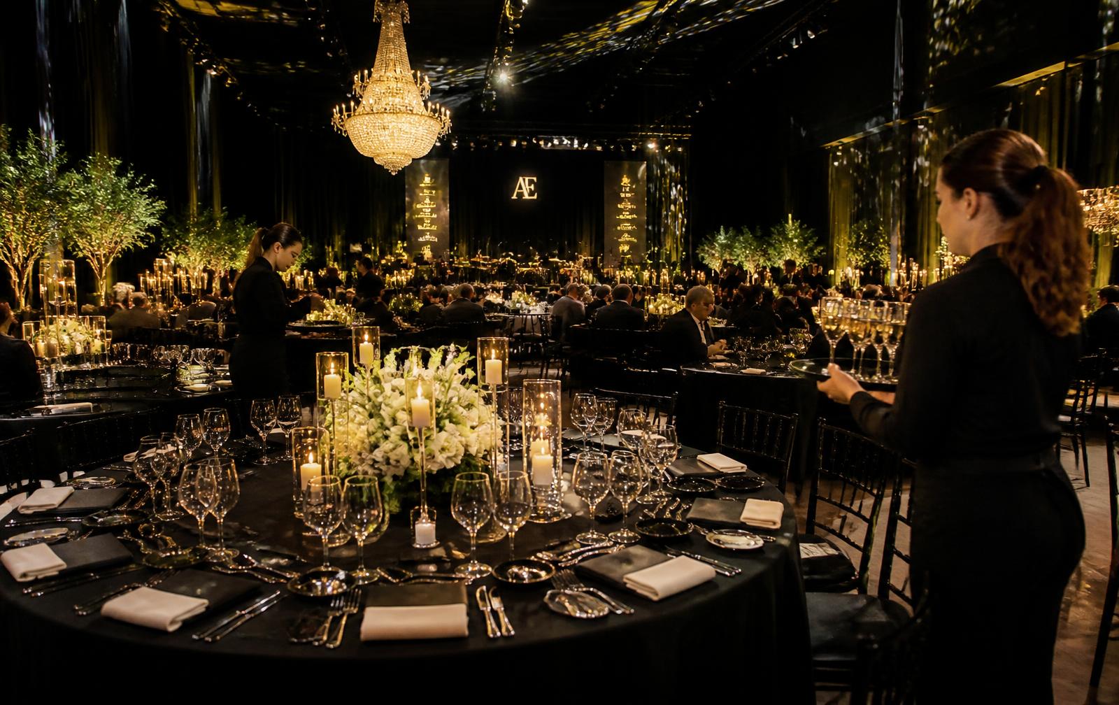 Salón de gala montado con vajilla, velas y personal de servicio atendiendo a los invitados